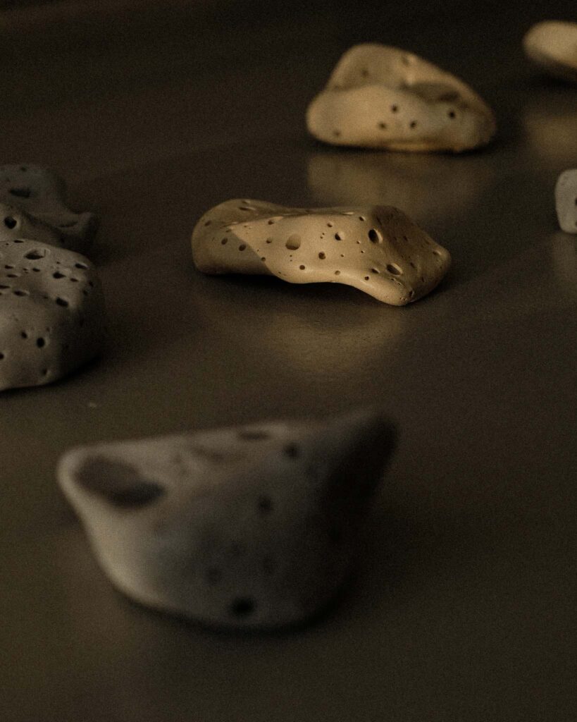 Ondou studio slowmade ceramics Sculptural incense pebble burners in dark and beige tones scattered on grey concrete, with sunlight creating soft, organic shadows.