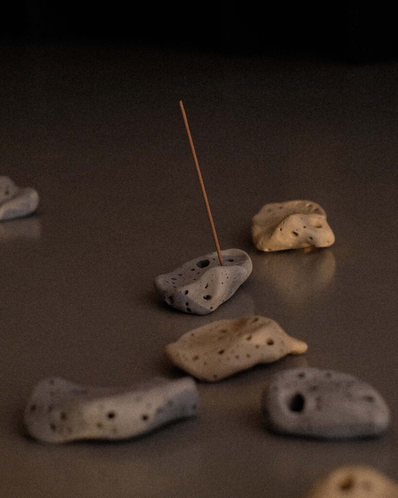 Ondou studio slowmade ceramics Sculptural incense pebble burners in dark and beige tones scattered on grey concrete, with sunlight creating soft, organic shadows.