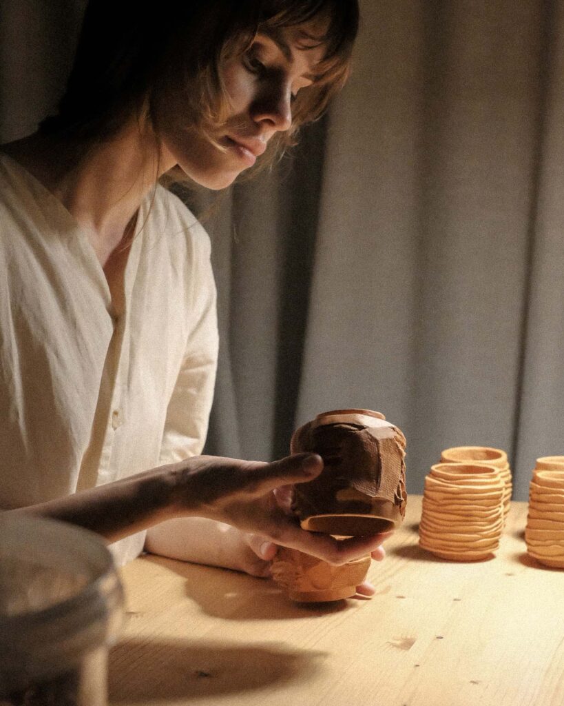 Ondou's creator, artist, and designer working on kurinuki cups in her studio, captured in soft evening light, evoking a tranquil, contemplative atmosphere.