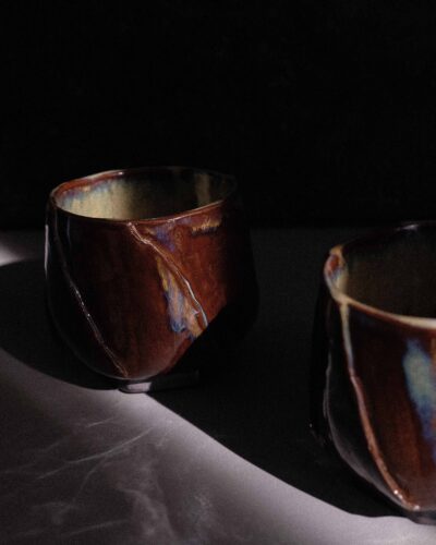 Hand-crafted Ondou Kurinuki Cup Nº9 made from black stoneware, with glossy iron brown-beige glaze in a dramatic contrasted light.