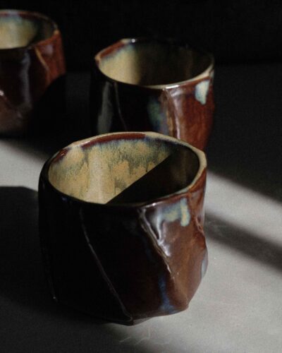 Hand-crafted Ondou Kurinuki Cup Nº9 made from black stoneware, with glossy iron brown-beige glaze in a dramatic contrasted light.