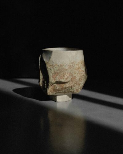 Sculptural Ondou kurinuki cup no.12 from light beige clay, strongly carved and decorated with local wild clay and sand mixture. Photographed in a dramatic light against the dark background.