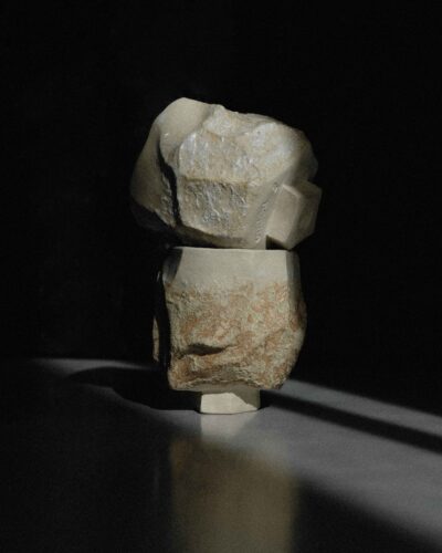 Sculptural Ondou kurinuki cup no.12 from light beige clay, strongly carved and decorated with local wild clay and sand mixture. Photographed in a dramatic light against the dark background.