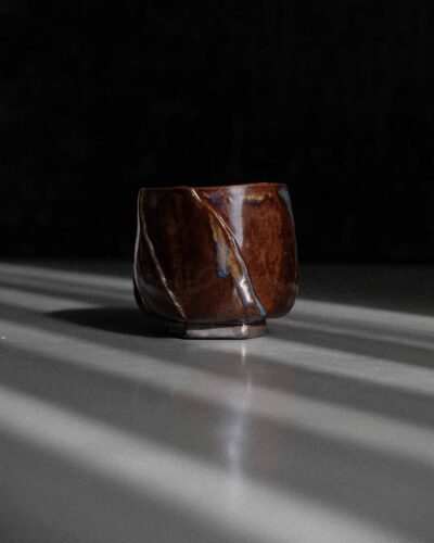 Hand-crafted Ondou Kurinuki Cup Nº9 made from black stoneware, with glossy iron brown-beige glaze in a dramatic contrasted light.