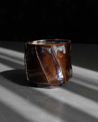 Hand-crafted Ondou Kurinuki Cup Nº9 made from black stoneware, with glossy iron brown-beige glaze in a dramatic contrasted light.