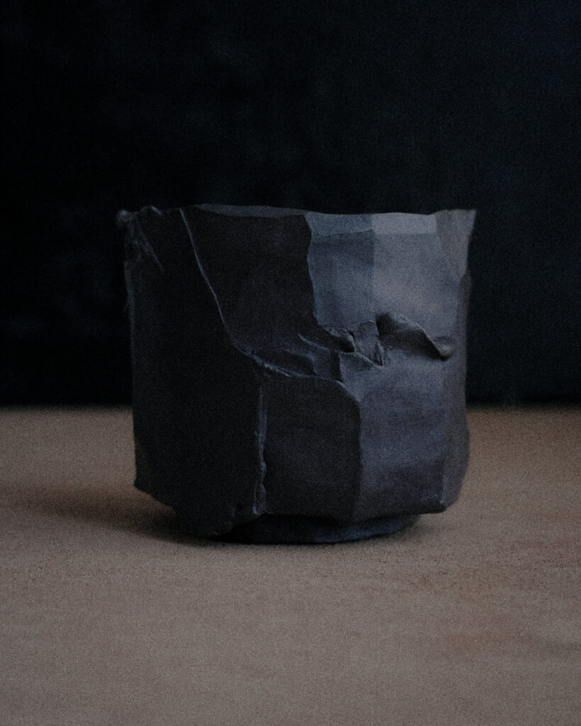 Large dark kurinuki stoneware vessel on natural kraft surface — sculptural handmade ceramic by Greta Rekštytė