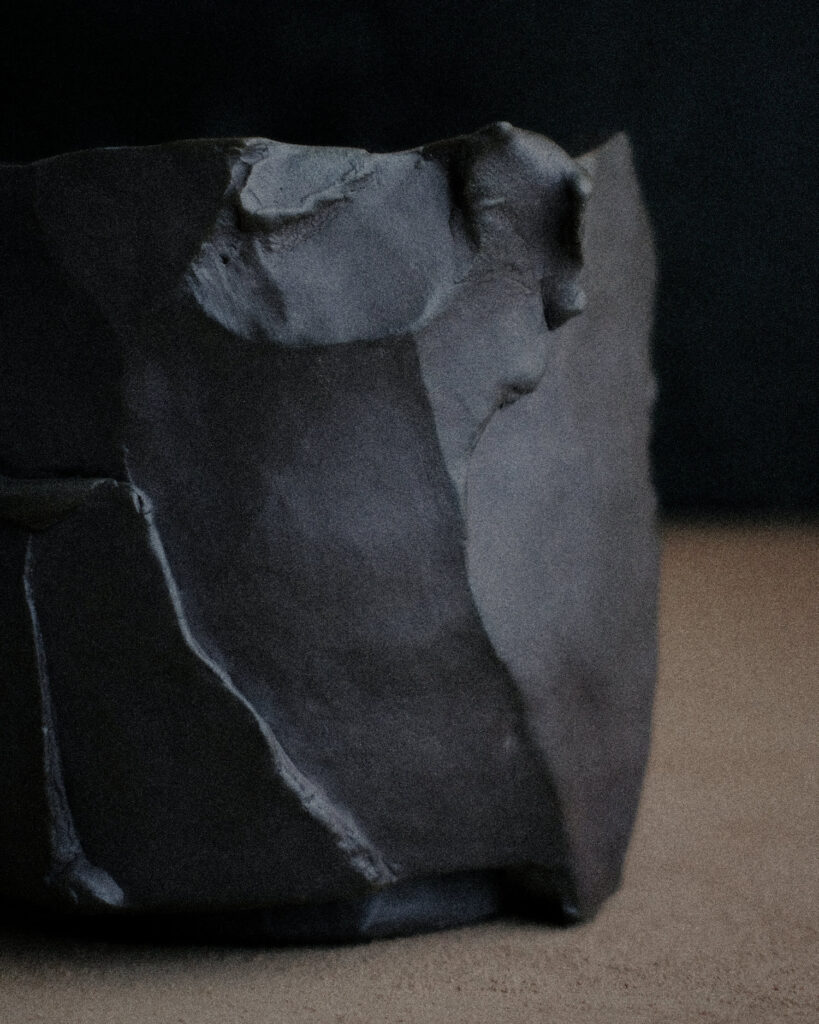 Faceted dark kurinuki vessel showing geometric carved planes and raw unglazed stoneware surface
